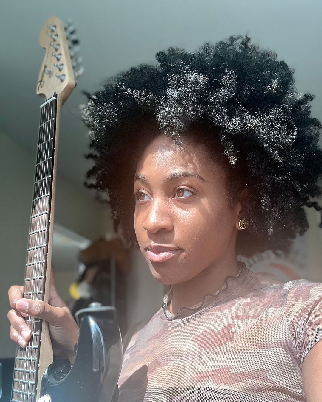 Alexis Moise poses seriously, staring ahead, holding a black guitar in her right hand 